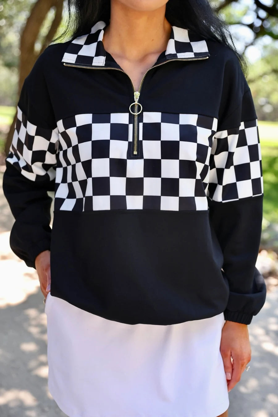 Person wearing a black and white checkered pullover with a blurred natural background