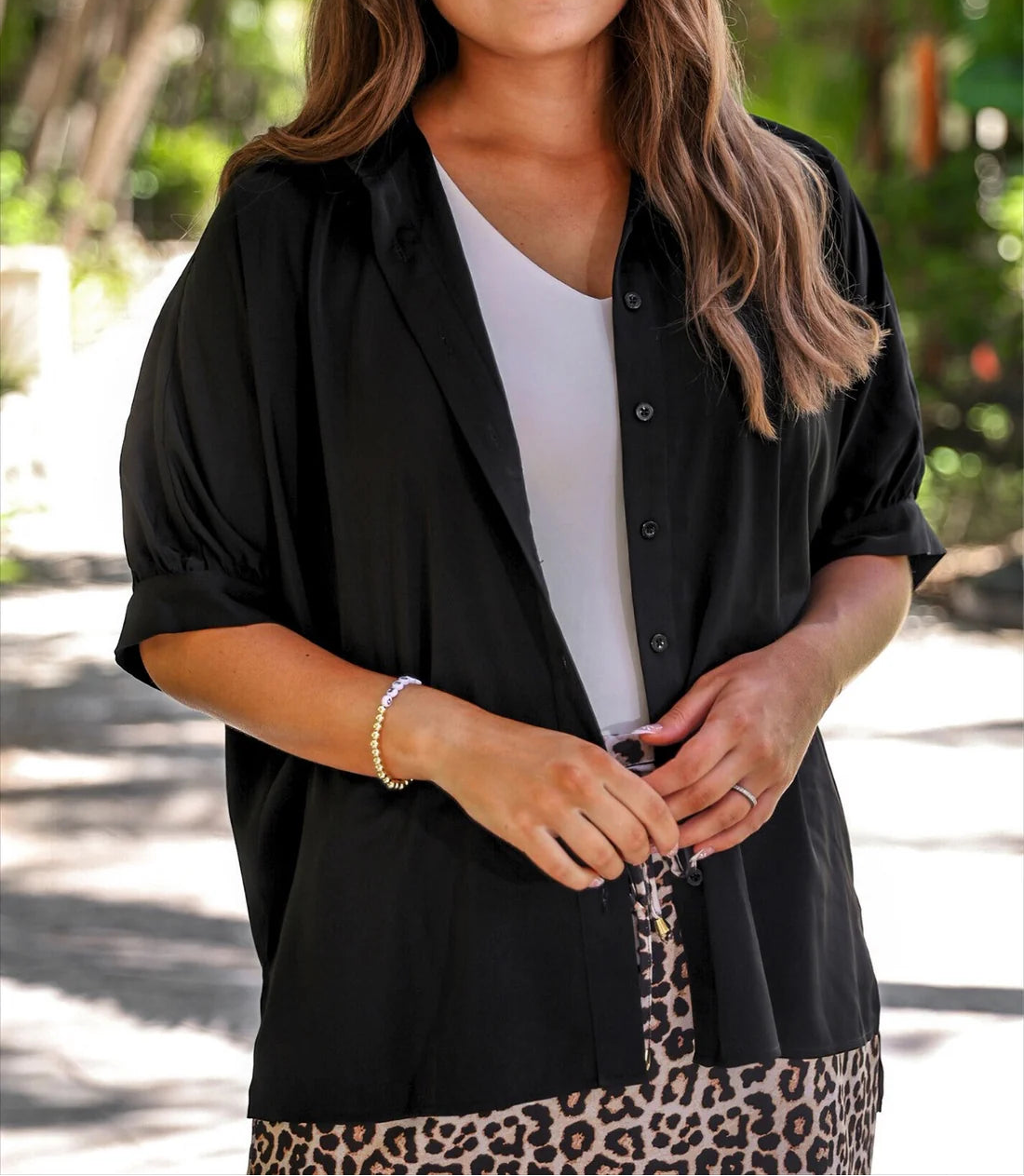 Person wearing a black shirt over a white top with a leopard print skirt outdoors.