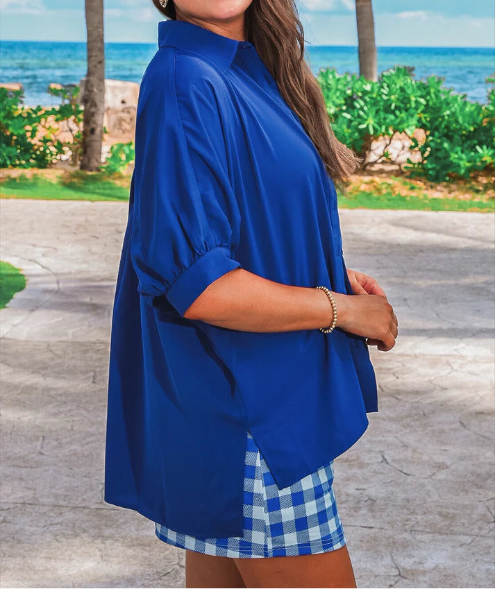 Woman in a blue outfit with sunglasses standing by a beach with palm trees.