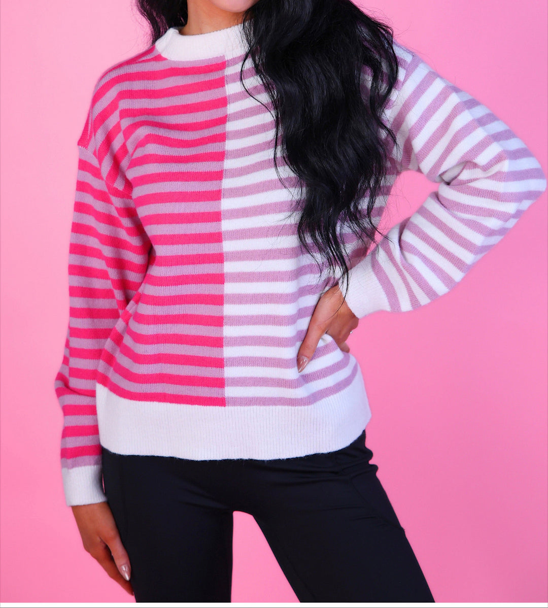 Woman wearing a pink and white striped sweater with long sleeves and black pants.