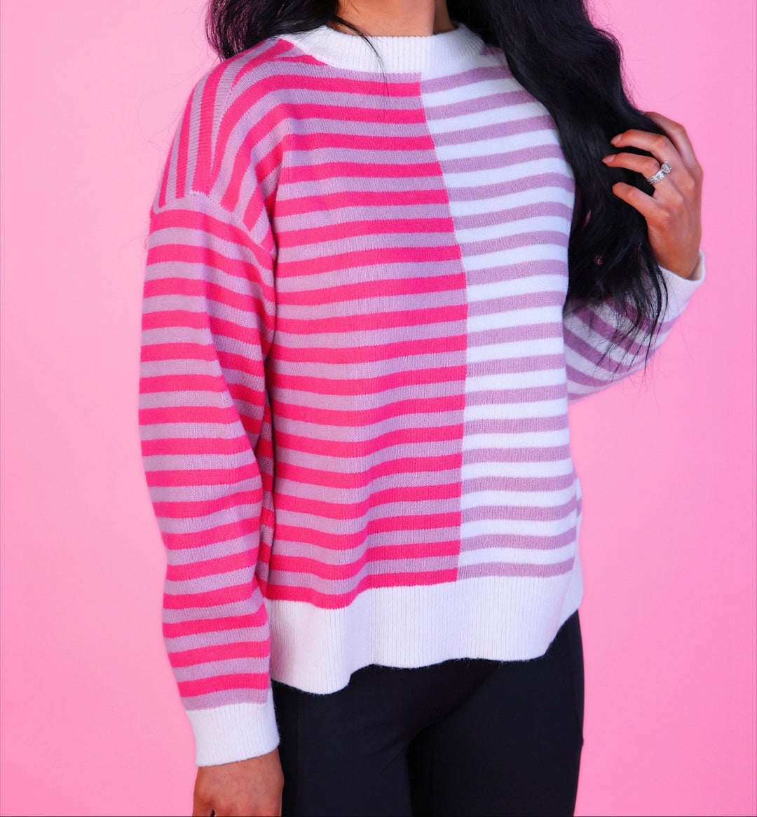Woman wearing a pink and white striped sweater with long sleeves and black pants.