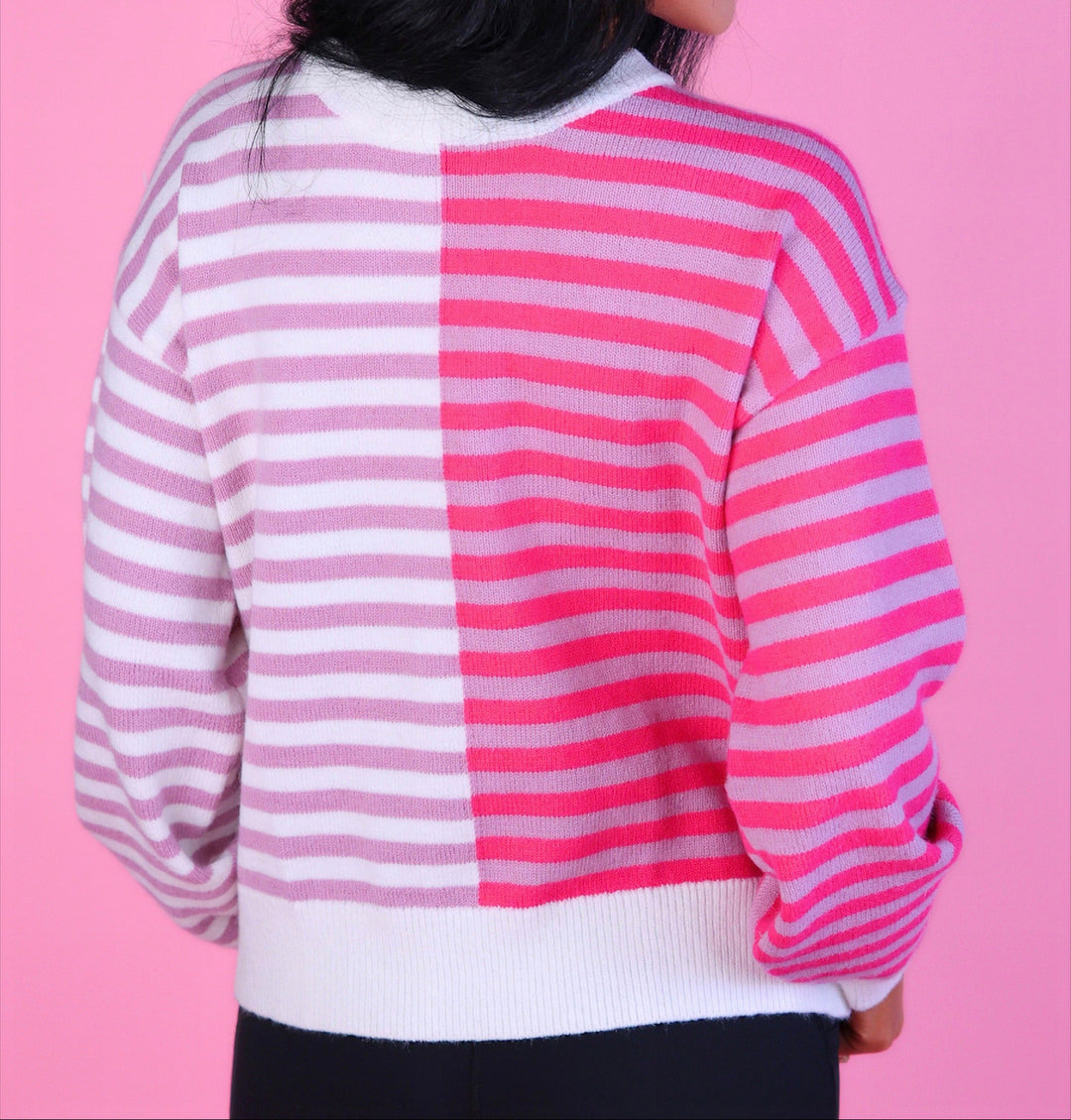 Woman wearing a pink and white striped sweater with long sleeves and black pants.