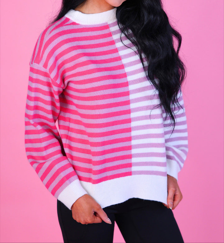 Woman wearing a pink and white striped sweater with long sleeves and black pants.