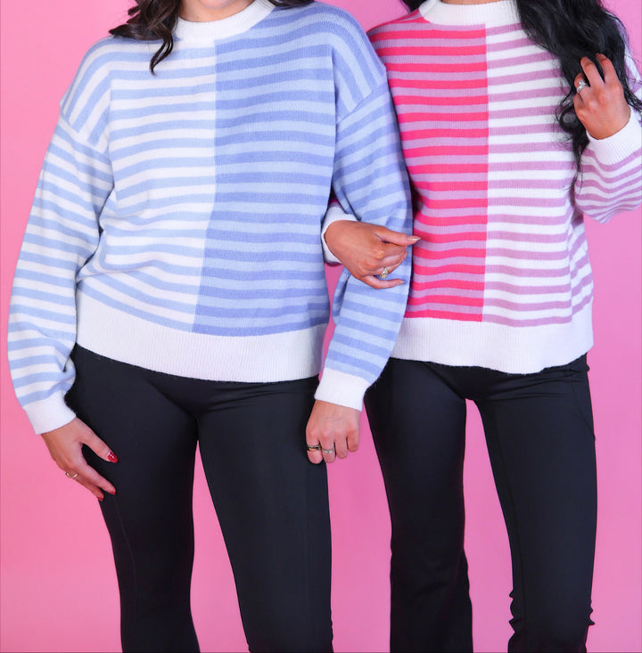 Woman wearing a pink and white and blue and white striped sweater with long sleeves and black pants.
