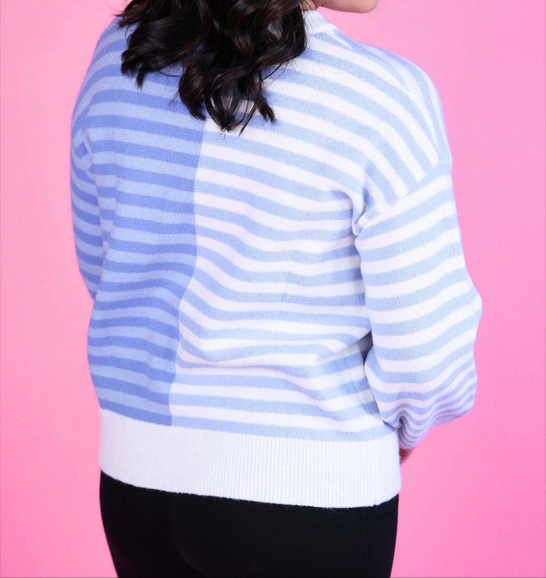 Woman wearing a blue and white striped sweater with long sleeves and black pants.