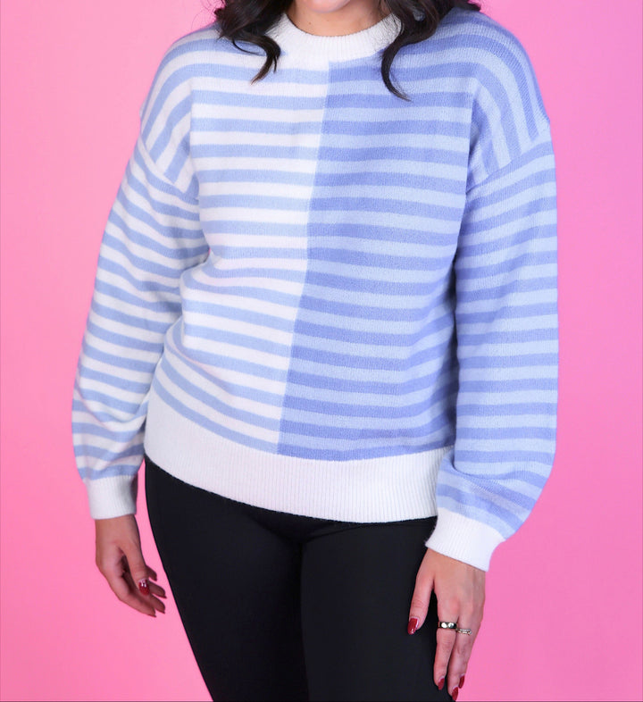 Woman wearing a blue and white striped sweater with long sleeves and black pants.