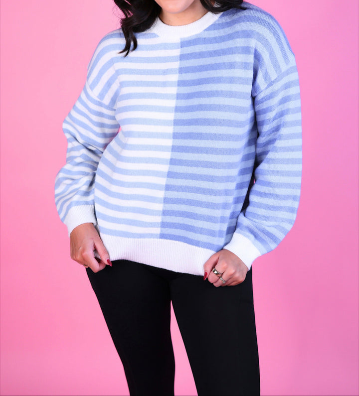 Woman wearing a blue and white striped sweater with long sleeves and black pants.