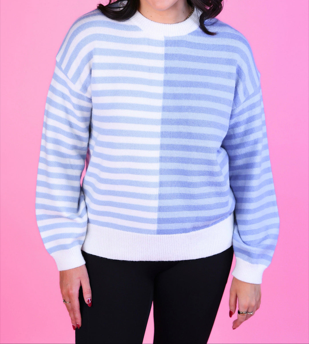 Woman wearing a blue and white striped sweater with long sleeves and black pants.