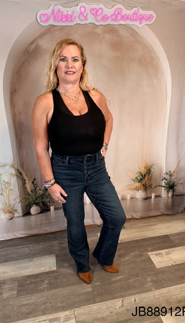 Woman in black tank top and blue jeans standing in a decorated room with 'Natali & Co Boutique' branding.