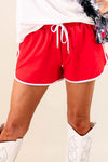 Red shorts with white drawstring and trim worn by a person on a beige background