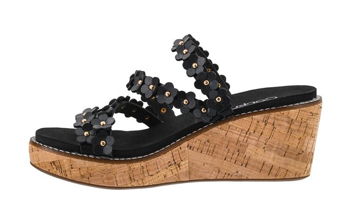 Black wedge sandal with floral embellishments on a cork platform against a white background