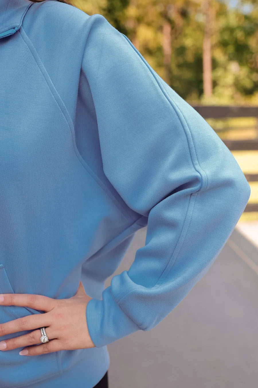 Close-up of a person wearing a light blue hoodie with a blurred outdoor background
