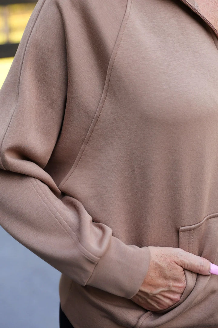 Close-up of a person wearing a mocha brown long-sleeve sweatshirt, showing the fabric texture, ribbed cuffs, and a hand in a pocket.