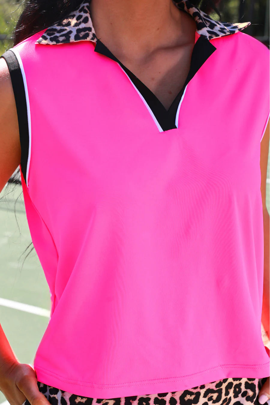 Person wearing a bright pink sleeveless top with black trim on a tennis court.