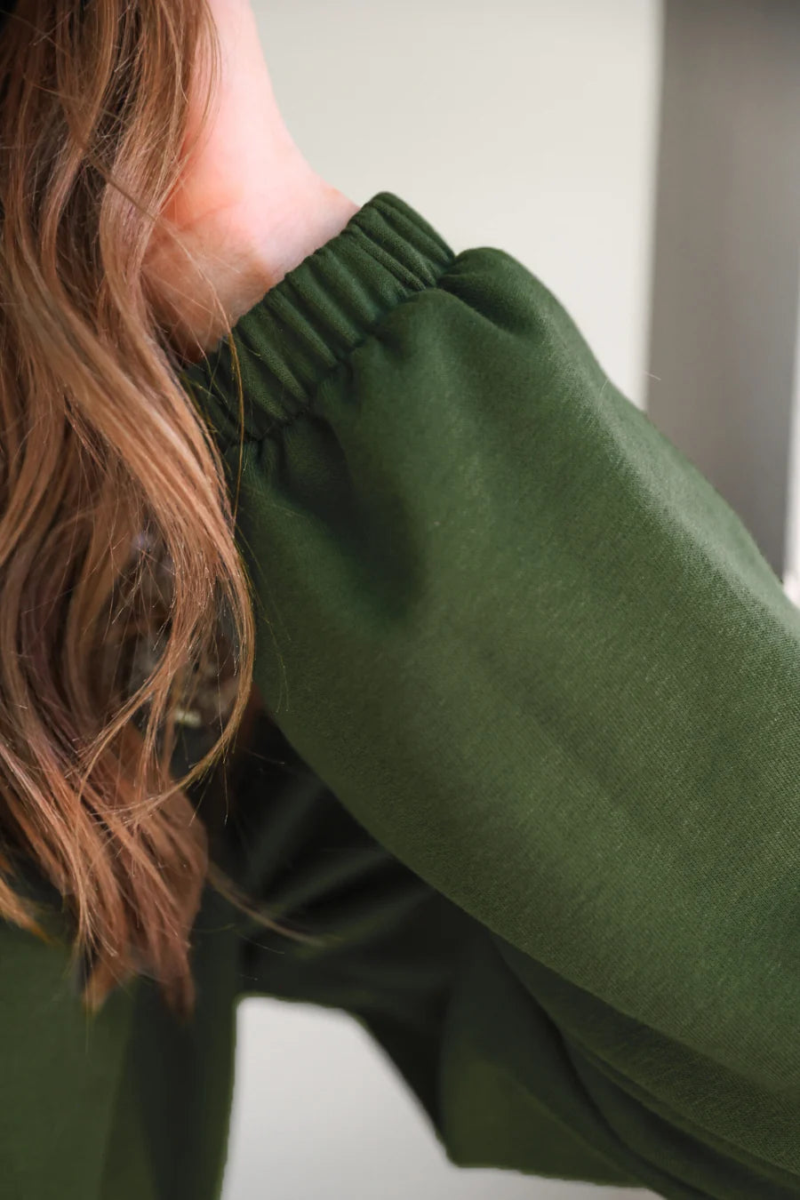Person wearing a green long-sleeve top with a blurred background