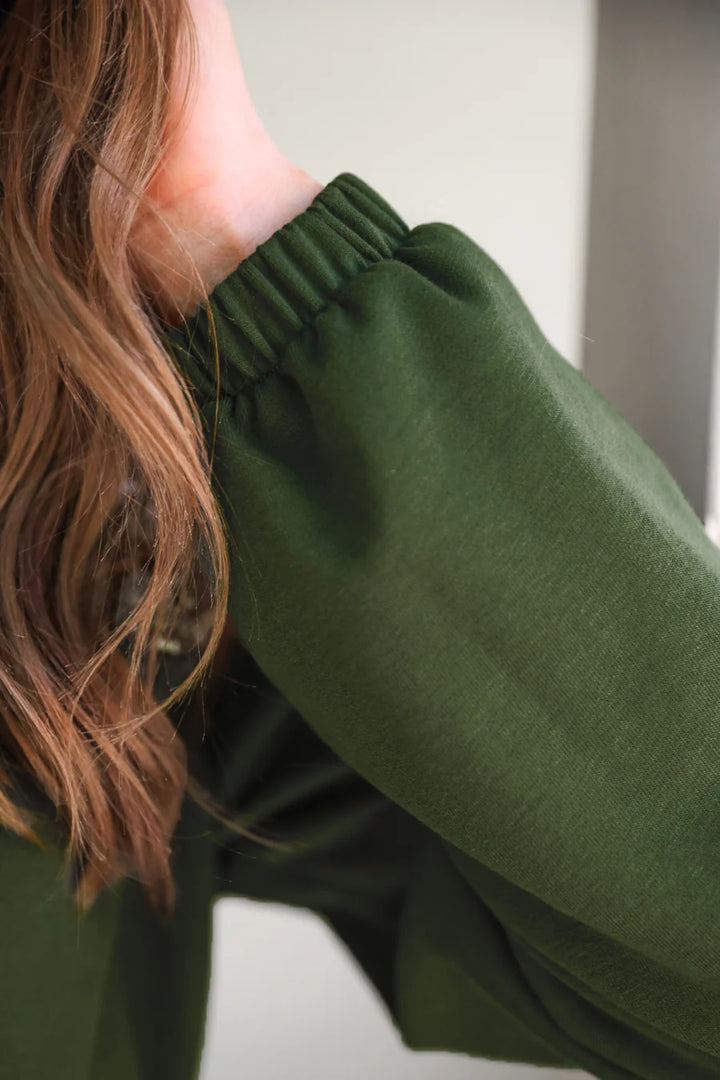 Person wearing a green long-sleeve top with a blurred background