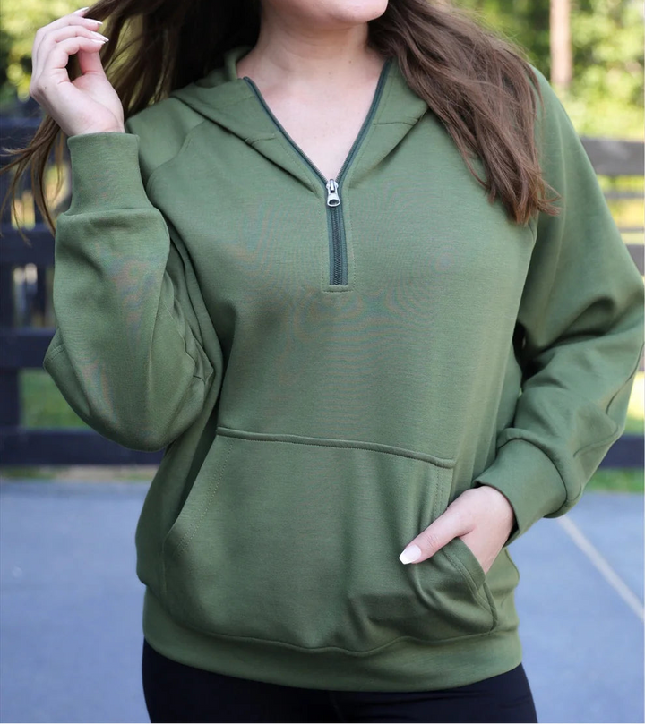 Woman wearing an olive zip-up hoodie outdoors with trees in the background