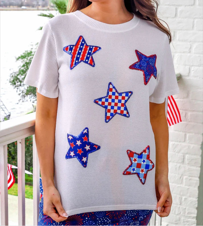 Woman wearing a white T-Top with red, white, and blue star patterns on a balcony.