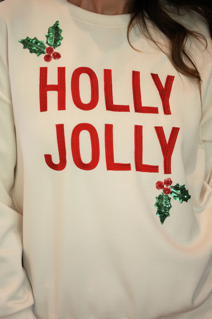 A close-up of a person wearing a cream-colored crewneck sweatshirt with &