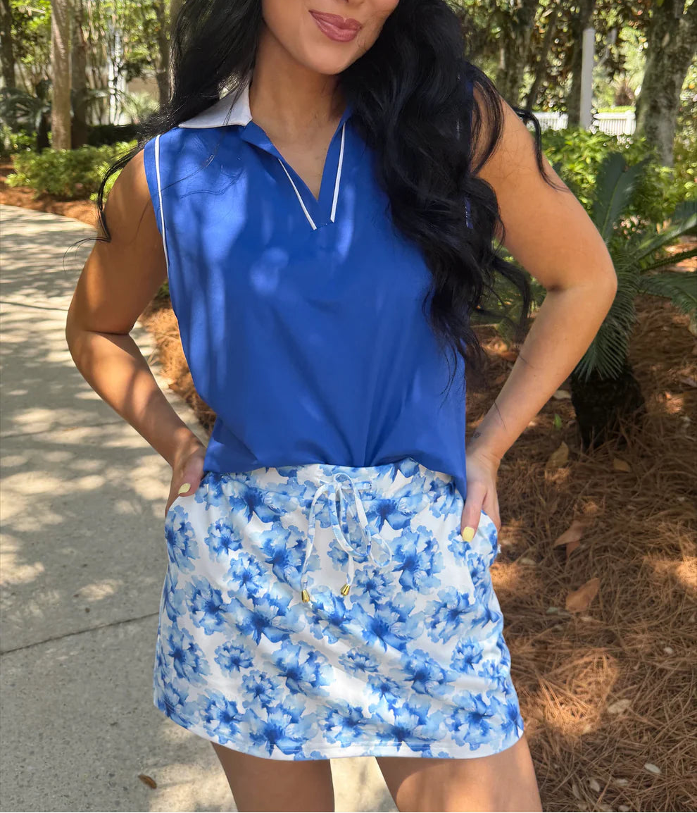 Woman wearing a blue sleeveless top and floral skort outdoors.