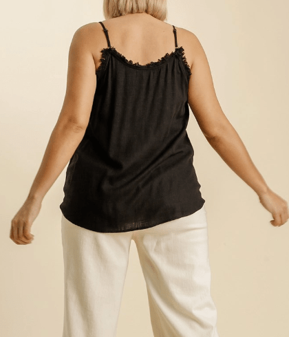 Person wearing a black tank top with thin straps and white pants on a beige background