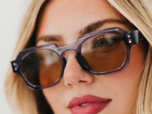 Close-up of a person wearing round sunglasses with a neutral background