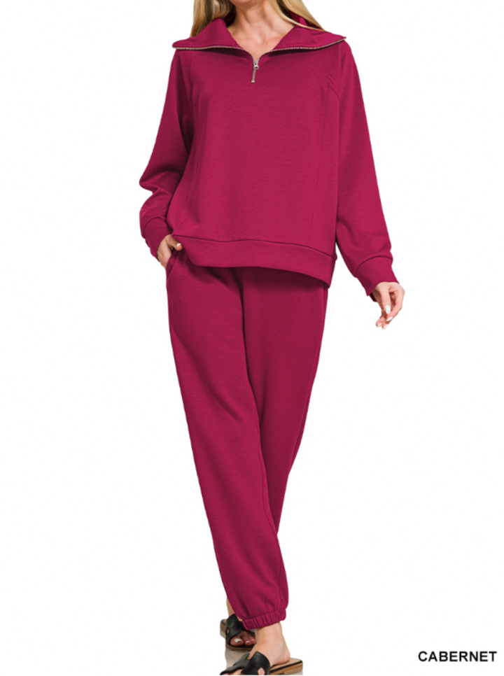 A woman modeling a matching two-piece lounge set in a deep cabernet pink color, featuring a quarter-zip long-sleeve top and jogger pants, against a plain white background.