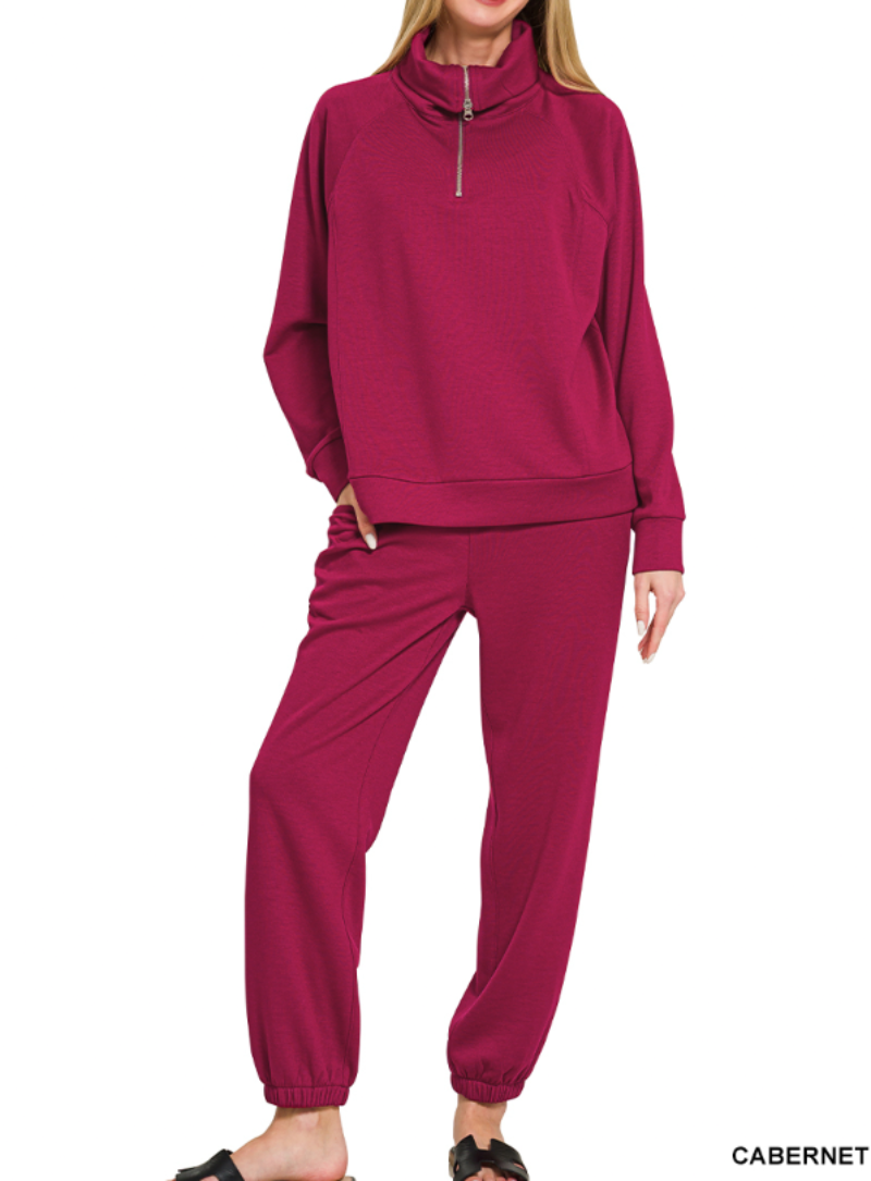  woman modeling a matching two-piece lounge set in a deep cabernet pink color, featuring a quarter-zip long-sleeve top and jogger pants, against a plain white background.