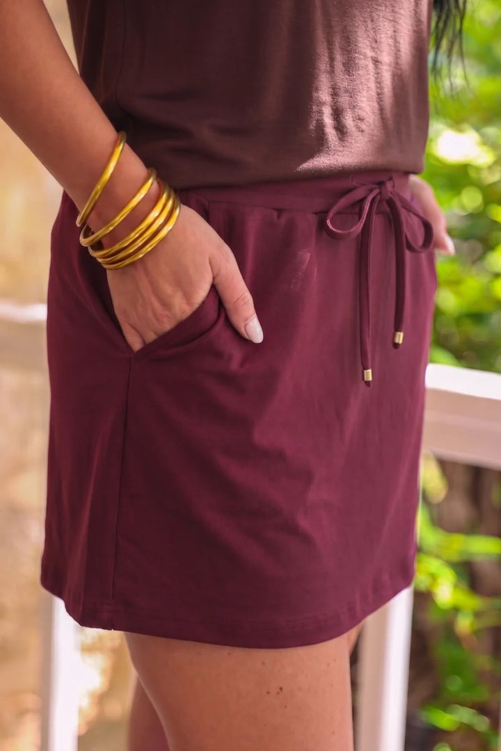 Person wearing a burgundy skort with gold bangles in front of a blurred green background