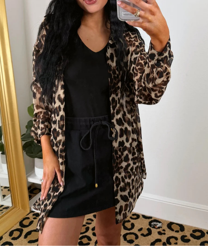 Woman taking a mirror selfie wearing a leopard print tunic over a black outfit.