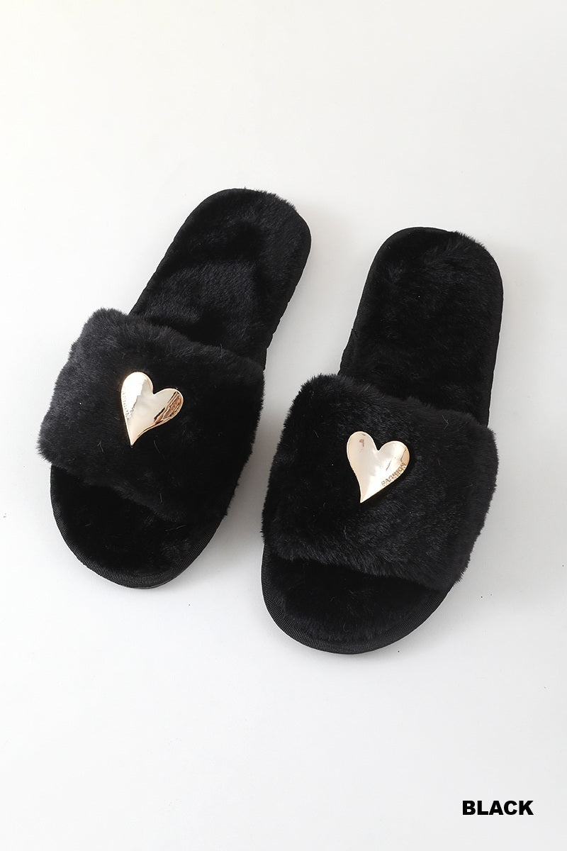 A pair of black fuzzy slide sandals with metallic gold heart-shaped embellishments on the straps, displayed on a clean white background with a &