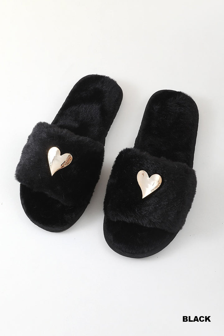 A pair of black fuzzy slide sandals with metallic gold heart-shaped embellishments on the straps, displayed on a clean white background with a &