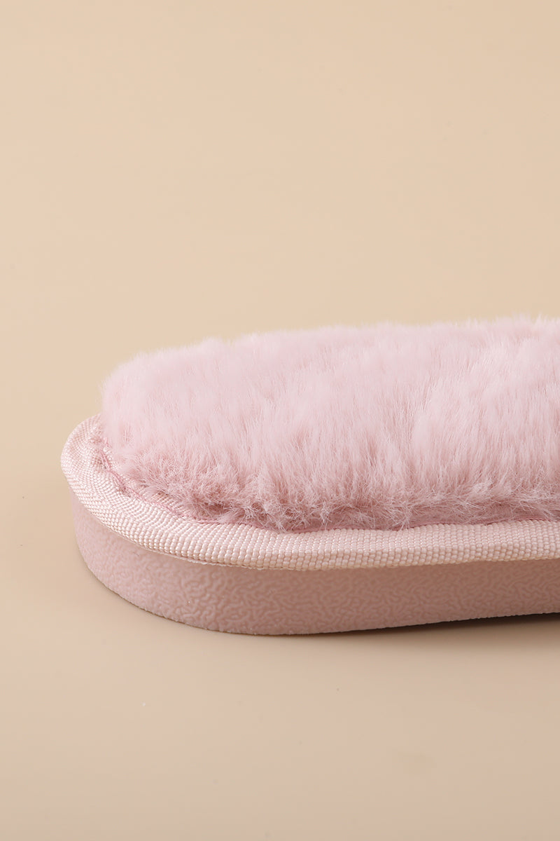 A close-up of a light pink fluffy faux-fur slippersurface with a matching pink fabric trim and sole, set against a solid beige background.