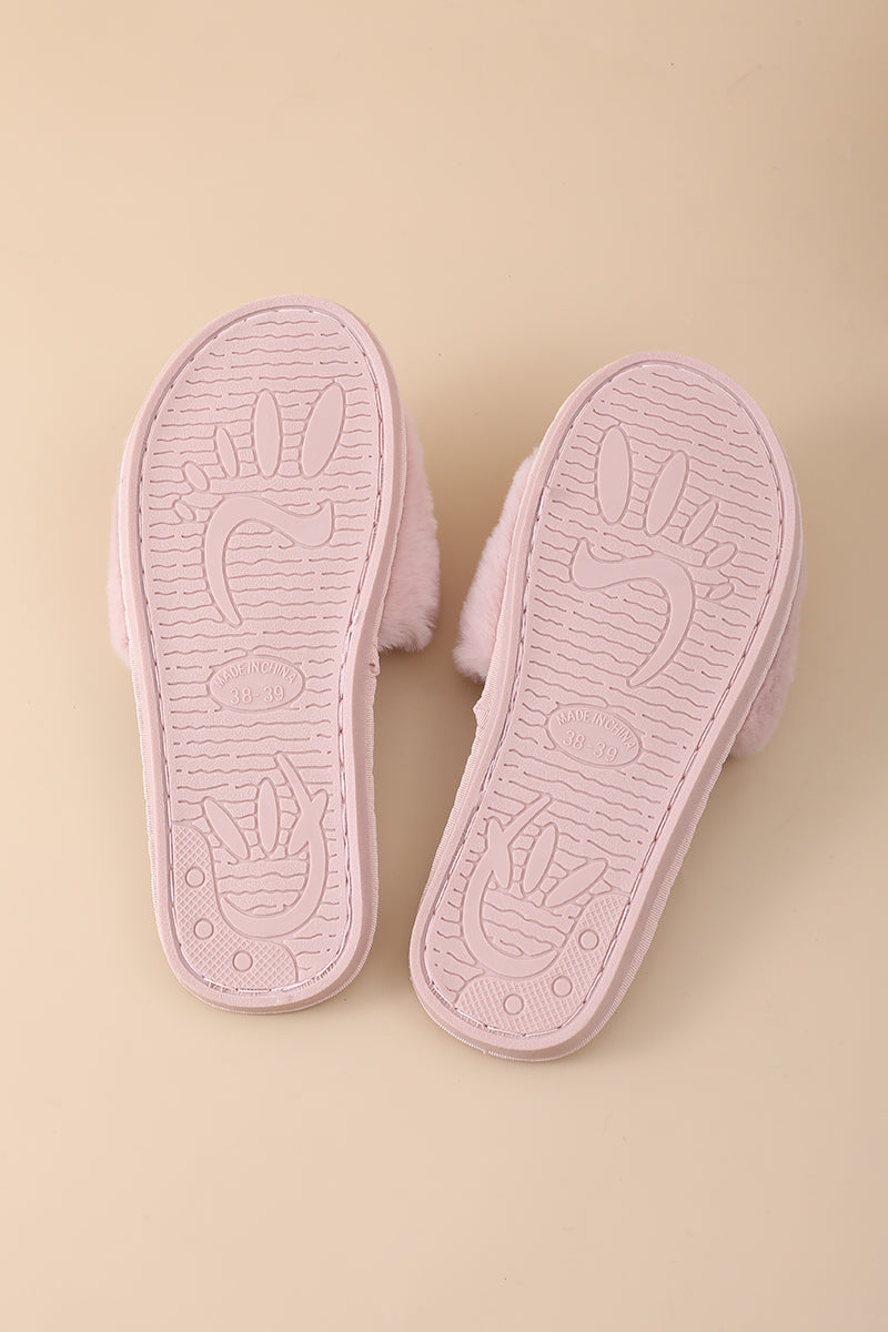 A pair of light pink slippers shown from the sole side, featuring a soft fuzzy texture and embossed bunny designs on a solid beige background.
