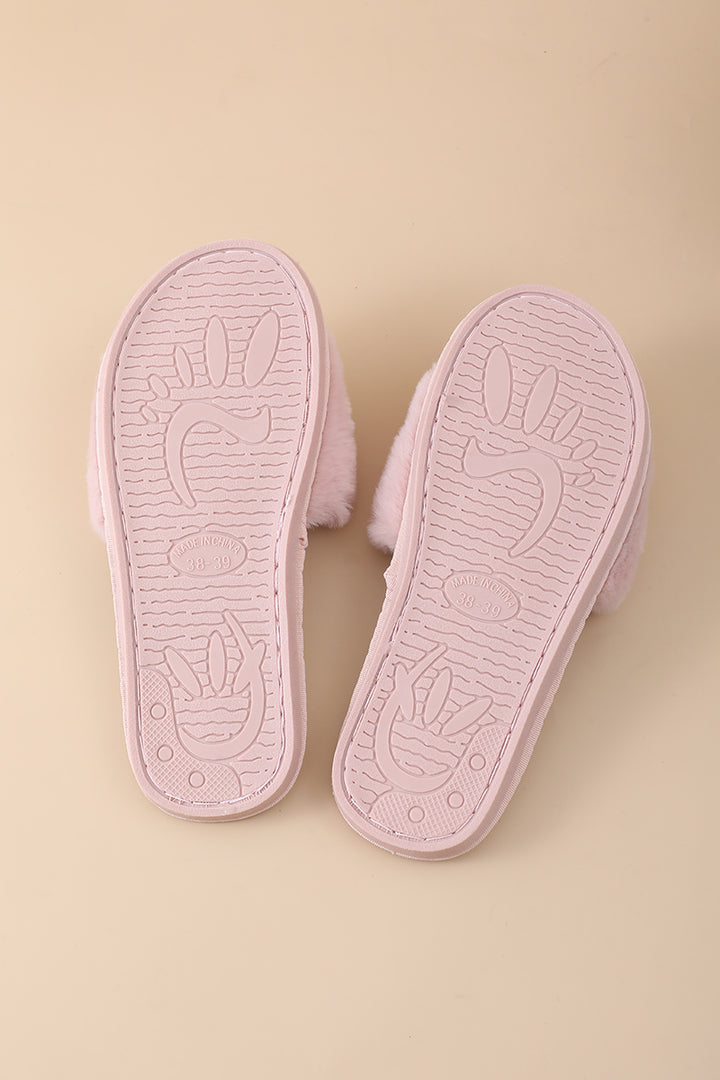 A pair of light pink slippers shown from the sole side, featuring a soft fuzzy texture and embossed bunny designs on a solid beige background.