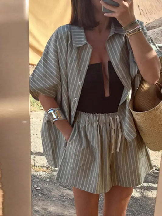 Person wearing a striped shirt and shorts with a brown top, holding a phone.