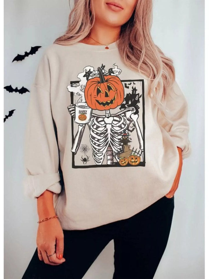Women wearing a beige sweatshirt with a skeleton with a pumpkin head holding a mug that says "Happy Halloween". Theres a scary house in the top right corner. a spider in the bottom left corner.
