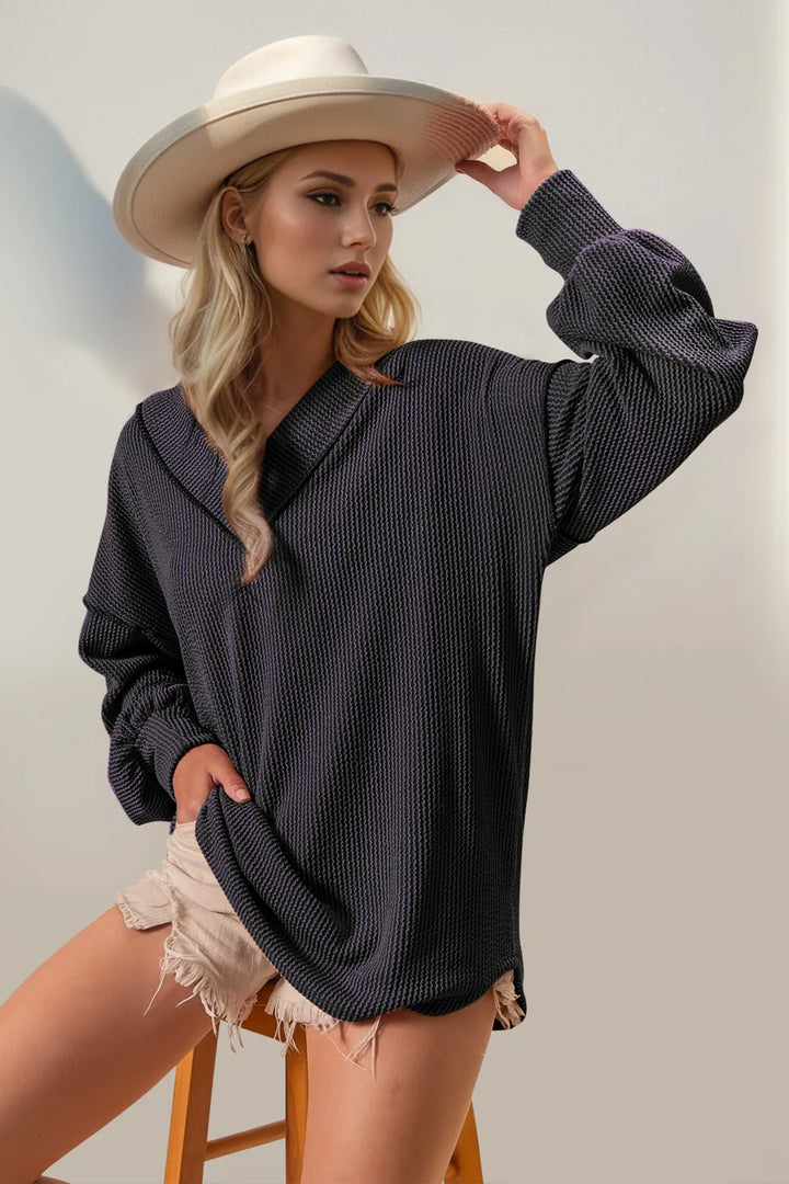 Woman wearing a dark gray oversized sweater and beige hat, standing on a stool against a plain background.