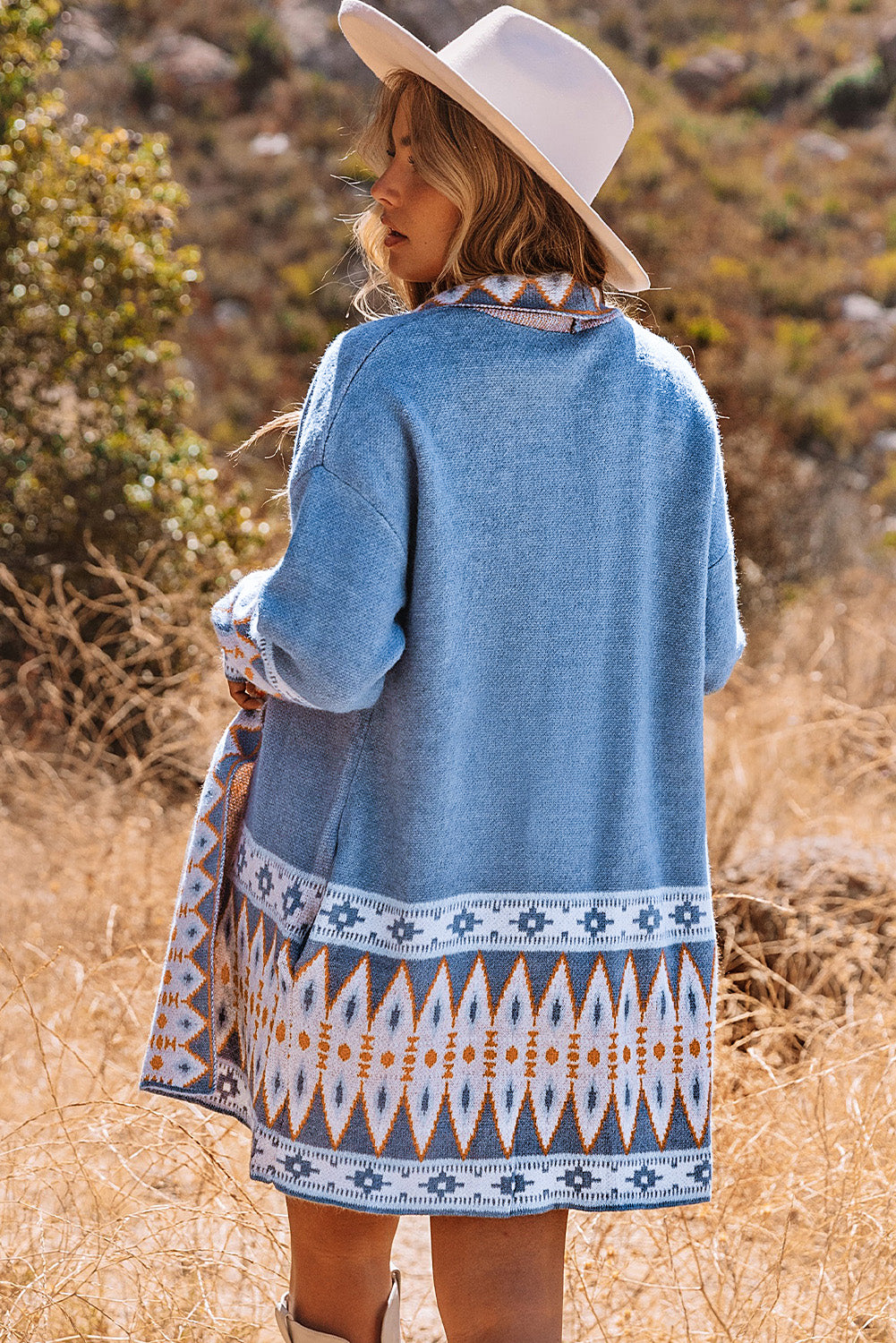 Woman wearing a blue patterned cardigan with a white hat in a natural setting