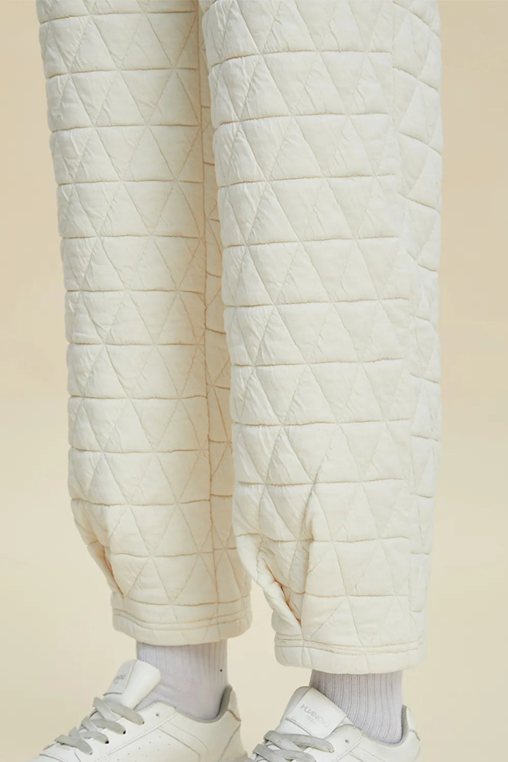Quilted white pants worn with white sneakers on a beige background