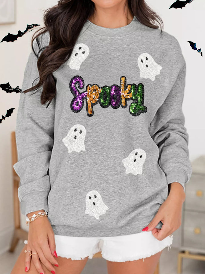 Women wearing grey sweatshirt with the word "Spooky" in purple, orange, and green sequence with 5 ghost flying around 