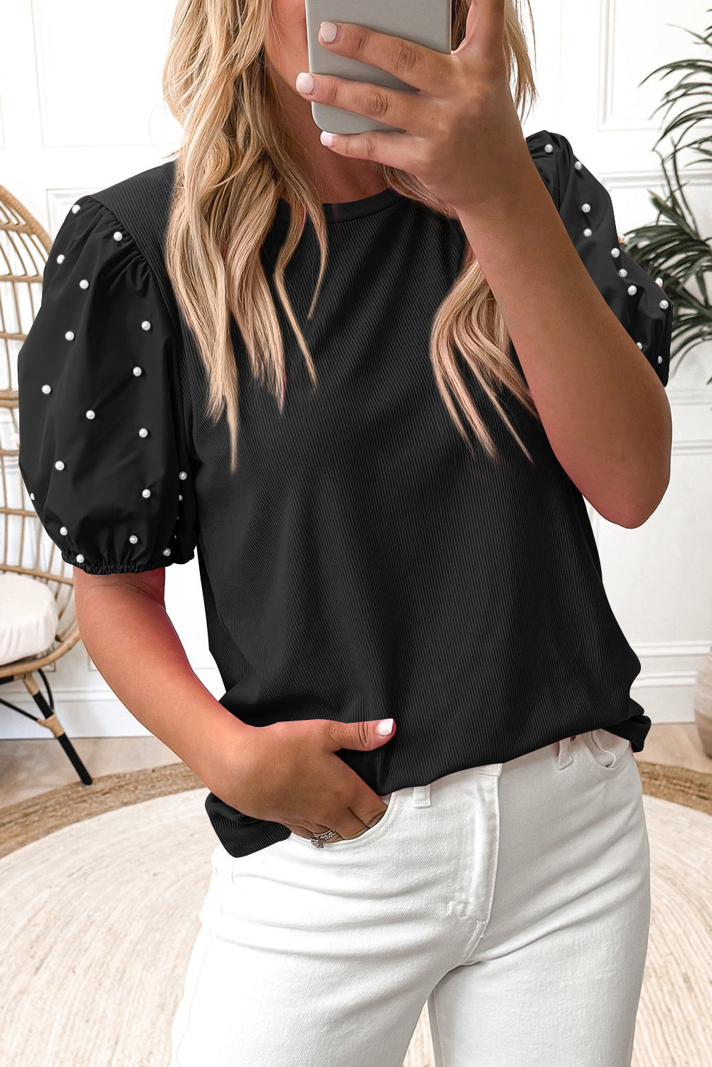 Person wearing a black top with white pearl dots and white pants indoors.