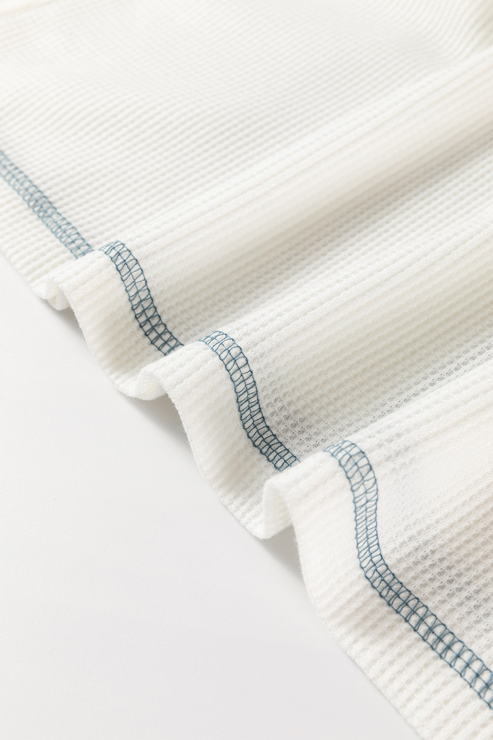 Close-up of a textured white fabric with blue stitching on a light gray background