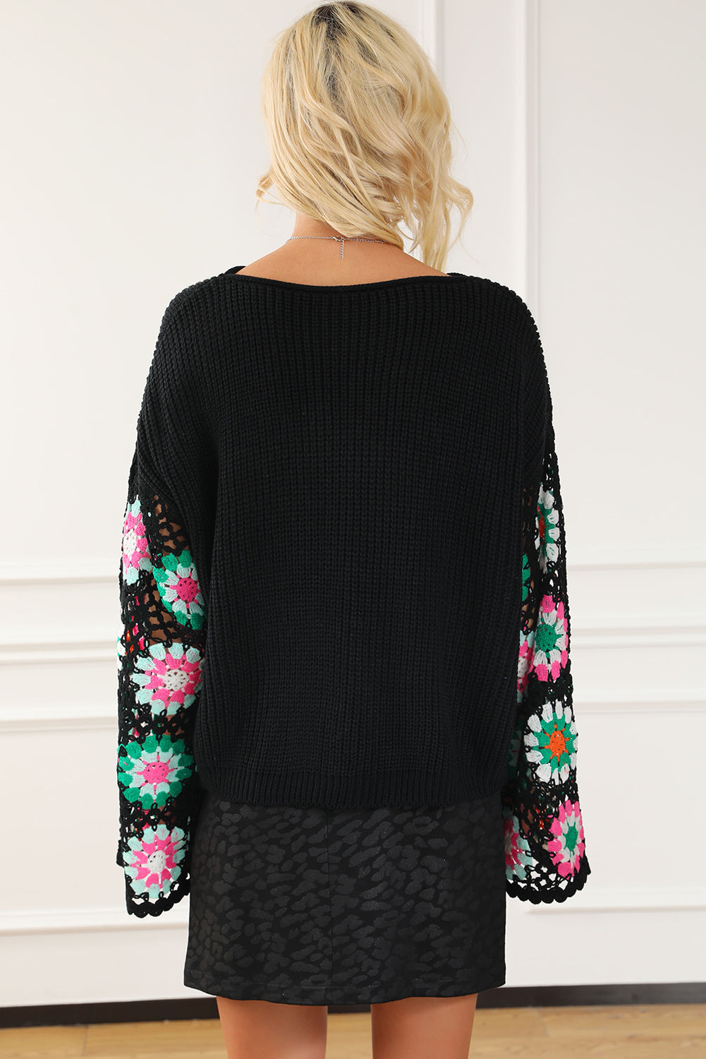 Black sweater with colorful floral patterns on sleeves against a white background