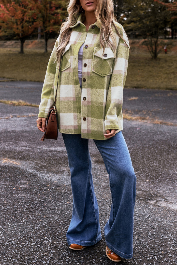 Person wearing a green plaid shirt and blue jeans standing on a paved surface with trees in the background.