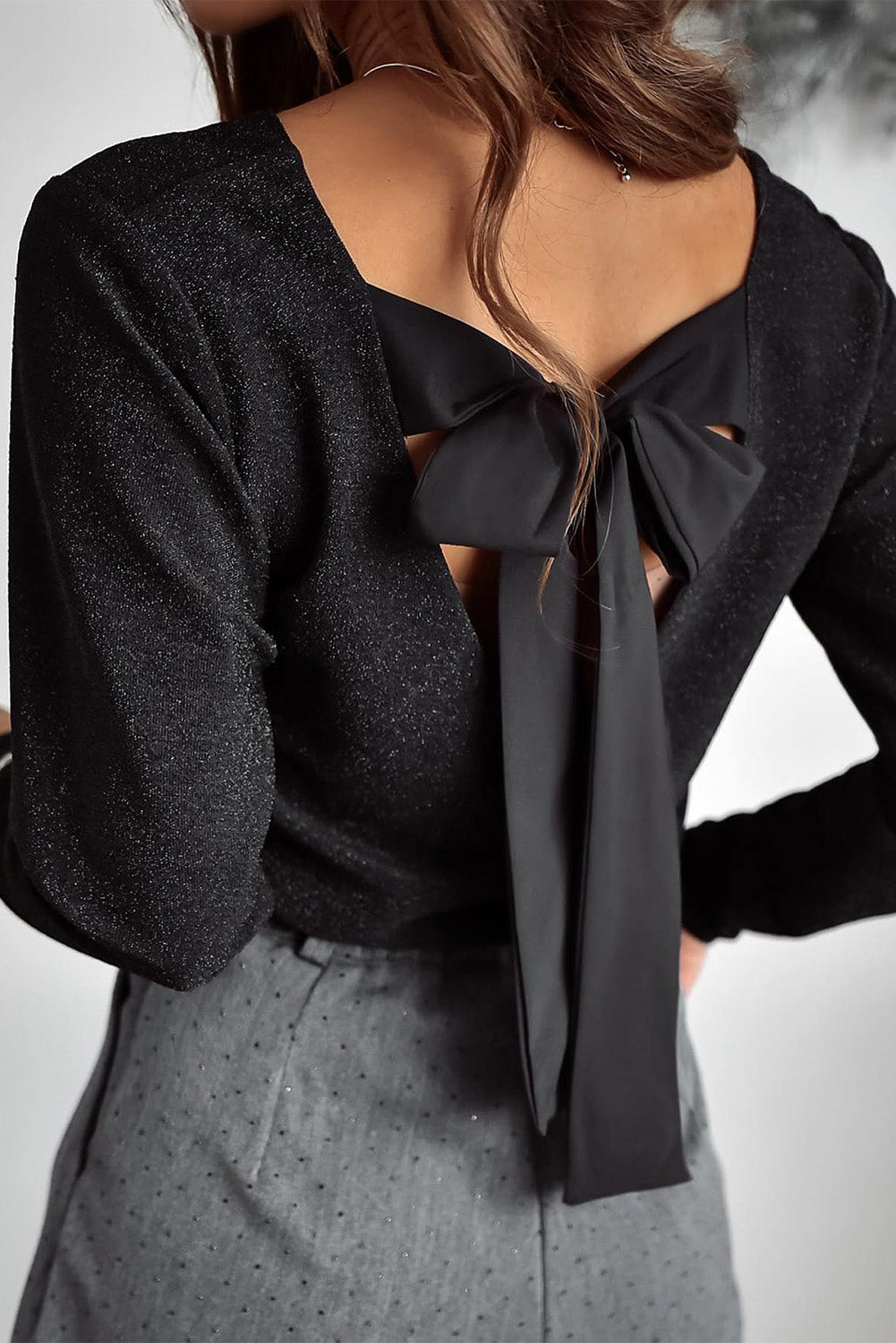 Black open-back top with a bow detail worn by a person on a neutral background