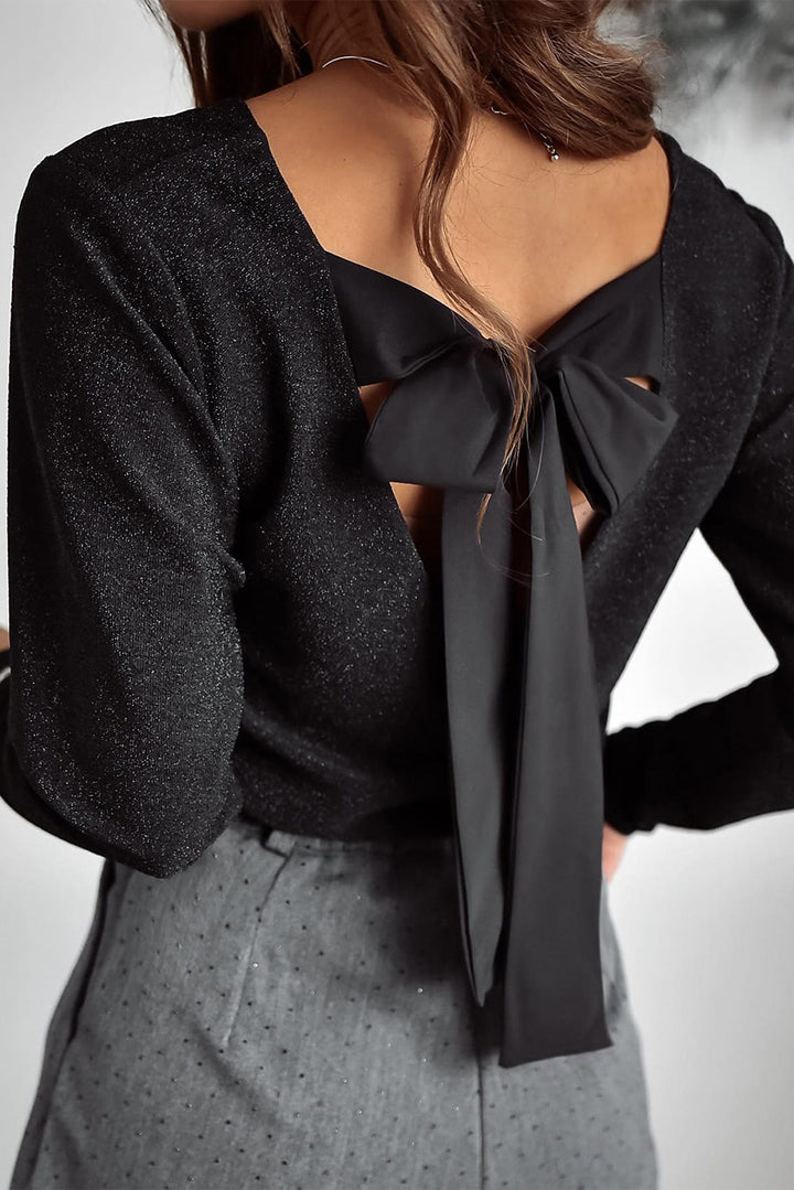Black open-back top with a bow detail worn by a person on a neutral background