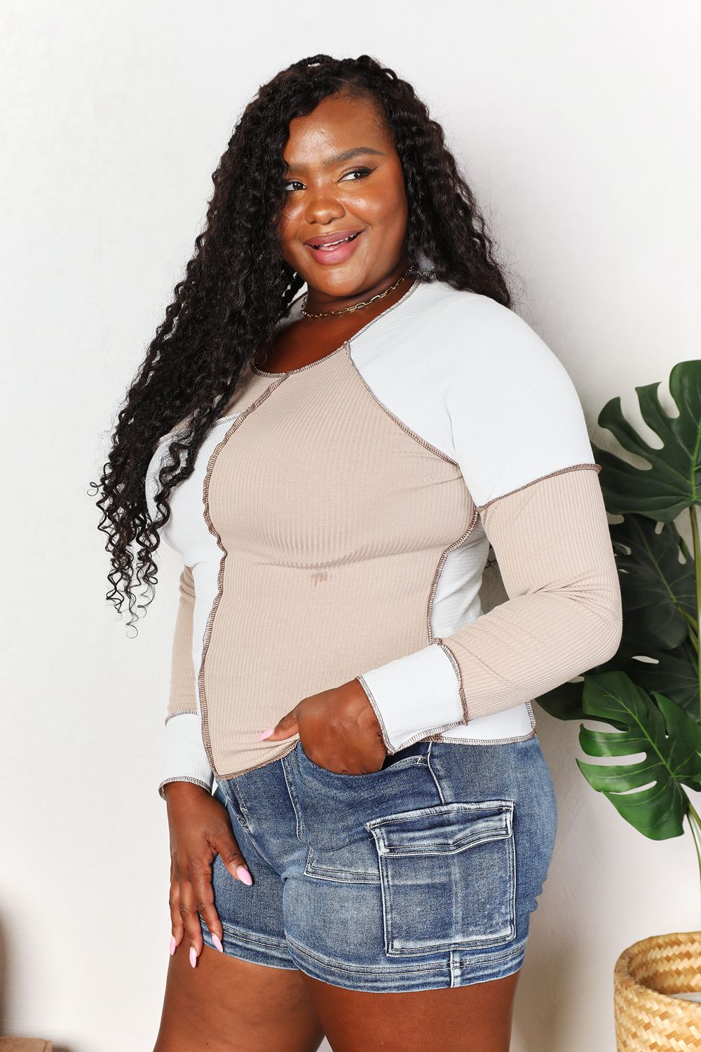 Woman wearing a beige and white long-sleeve top with denim shorts, standing indoors.