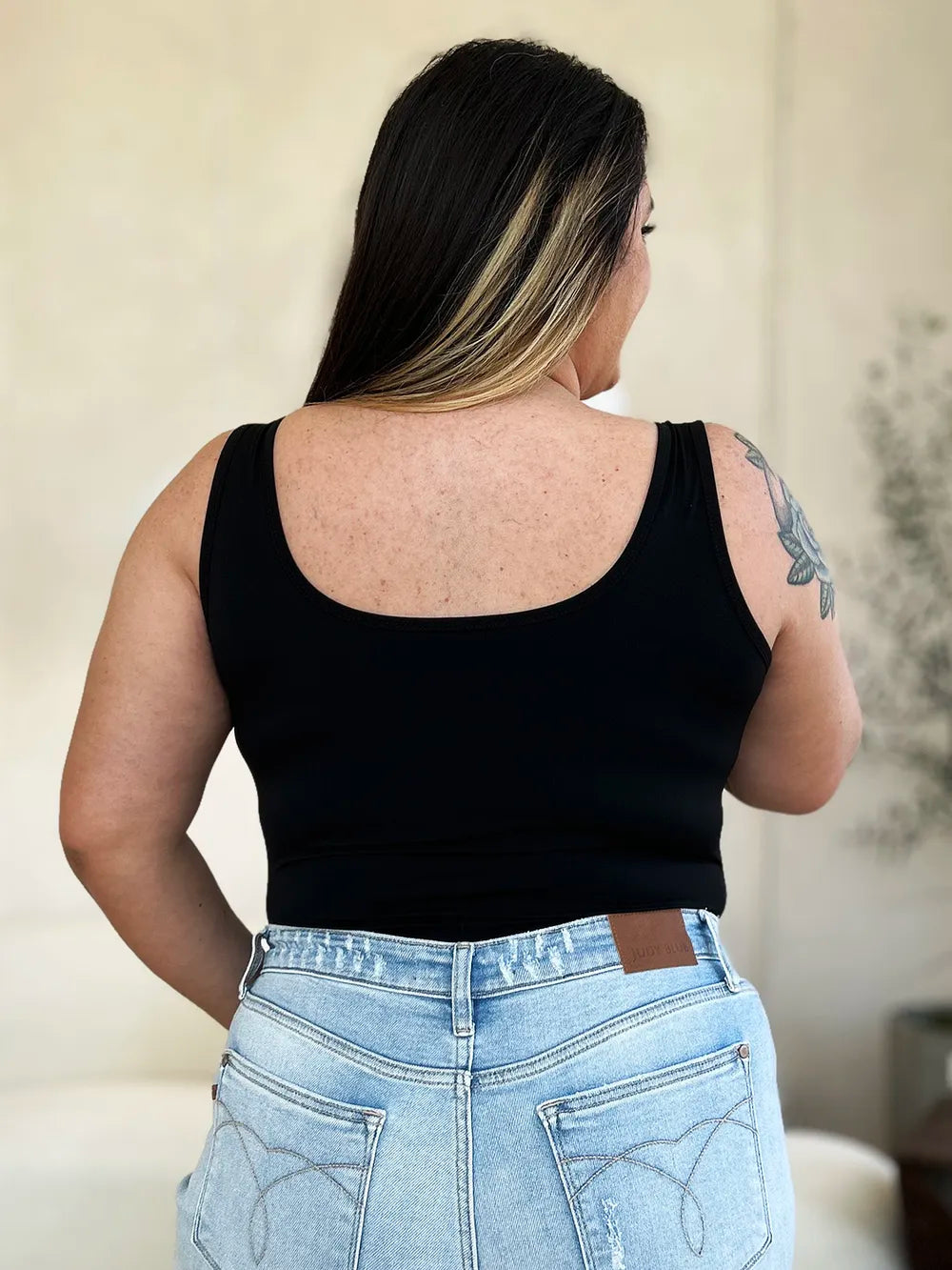 Person wearing a black tank top and light blue jeans with a neutral background
