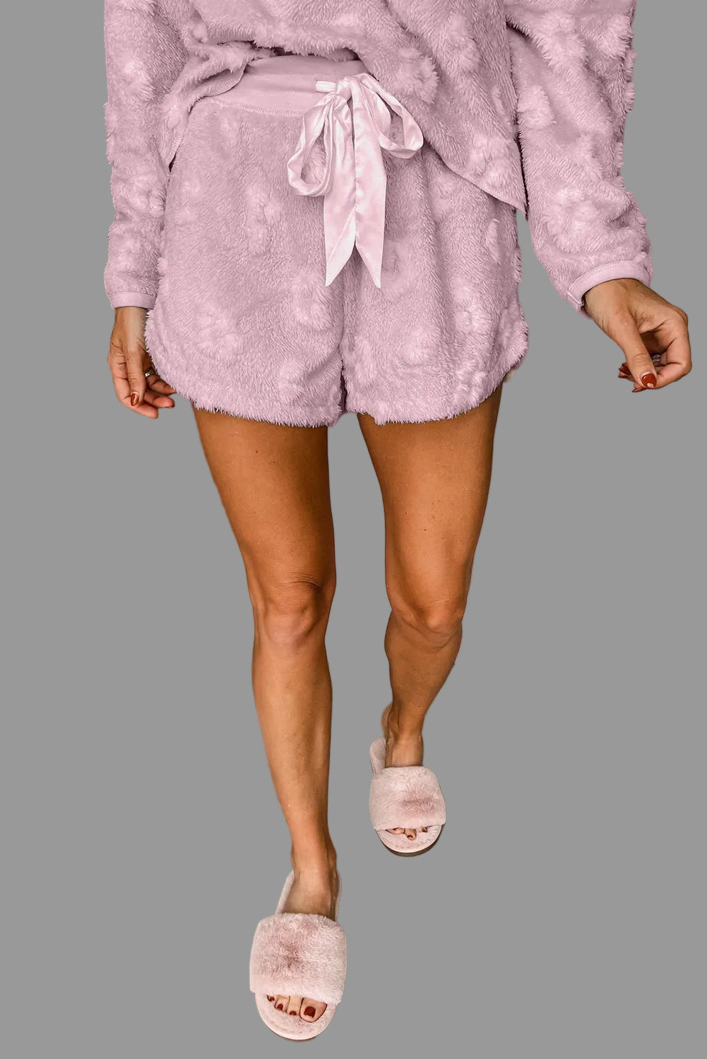 Person wearing a pink fleece outfit with shorts and a top, standing next to a gray wall.
